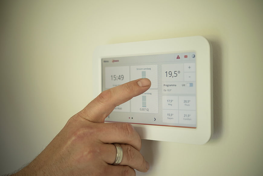 Man's hand touching smart home thermostat control panel on wall