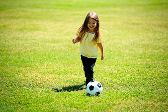 Happy little girl playing soccer on green grass field