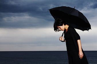 Melancholic woman with black umbrella by stormy sea