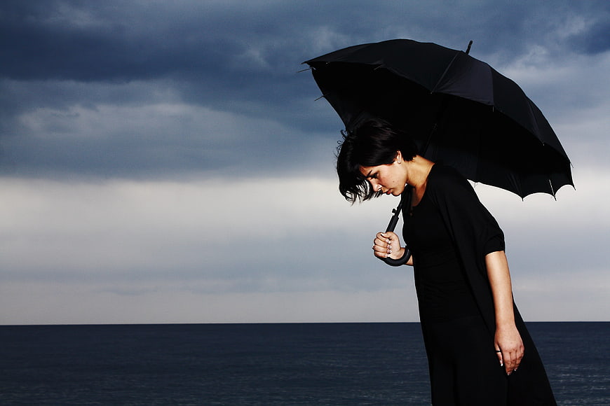 Melancholic woman with black umbrella by stormy sea