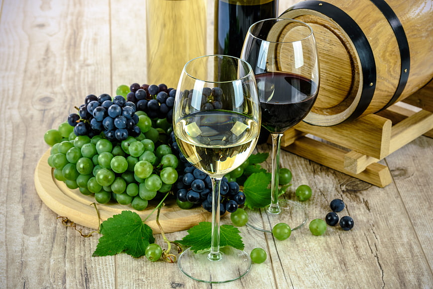 Red and white wine glasses with grapes and barrel
