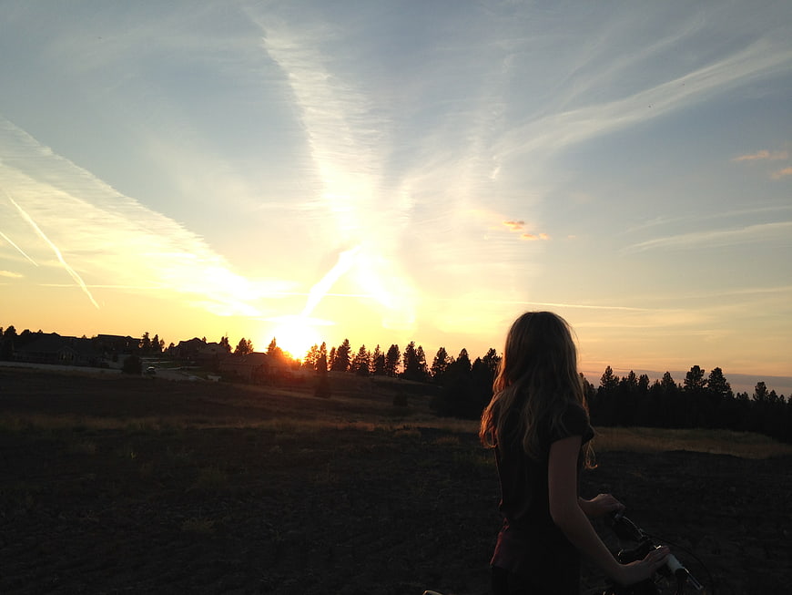 Woman on Bicycle Watching Golden Sunset Over Rural Hills