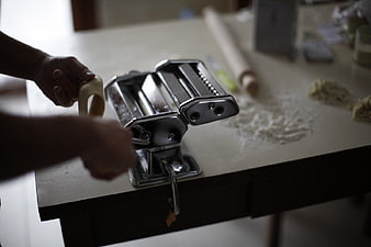 Hands Using Manual Pasta Maker Machine on Kitchen Table