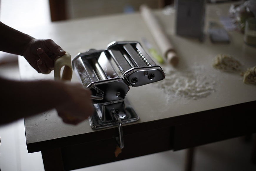 Hands Using Manual Pasta Maker Machine on Kitchen Table