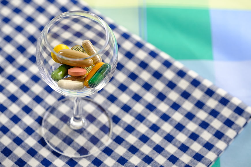 Colorful pills and capsules in a wine glass on a blue checkered tablecloth
