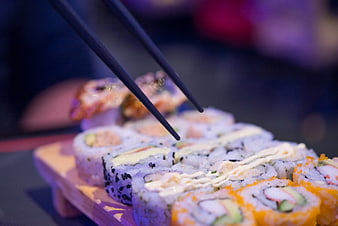 Close-up of sushi rolls with chopsticks on wooden board