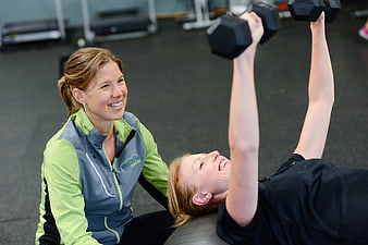 Personal trainer spotting woman lifting dumbbells in gym