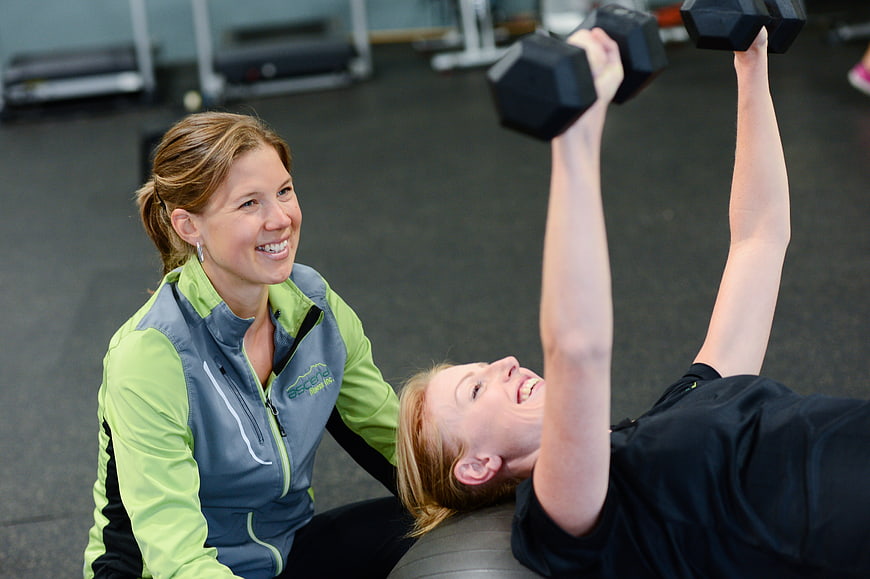 Personal trainer spotting woman lifting dumbbells in gym