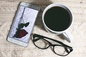 Flat lay of smartphone, coffee, and glasses on knitted blanket