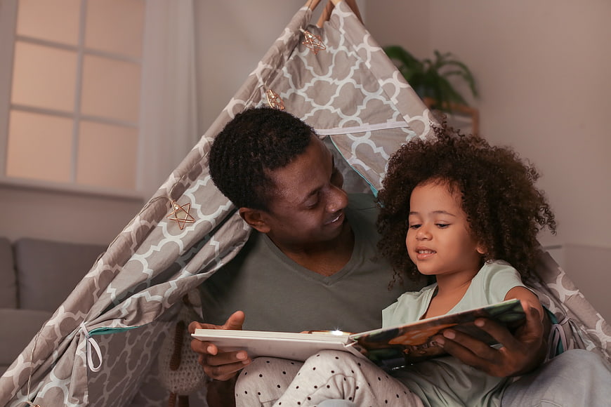 Father reading book to daughter in indoor tent