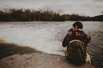 Photographer with Camera Sitting by Riverbank