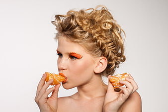 Creative Beauty Portrait of Woman Eating Mandarin with Orange Makeup