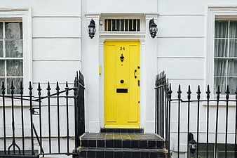 Bright yellow front door on white townhouse with black iron fence