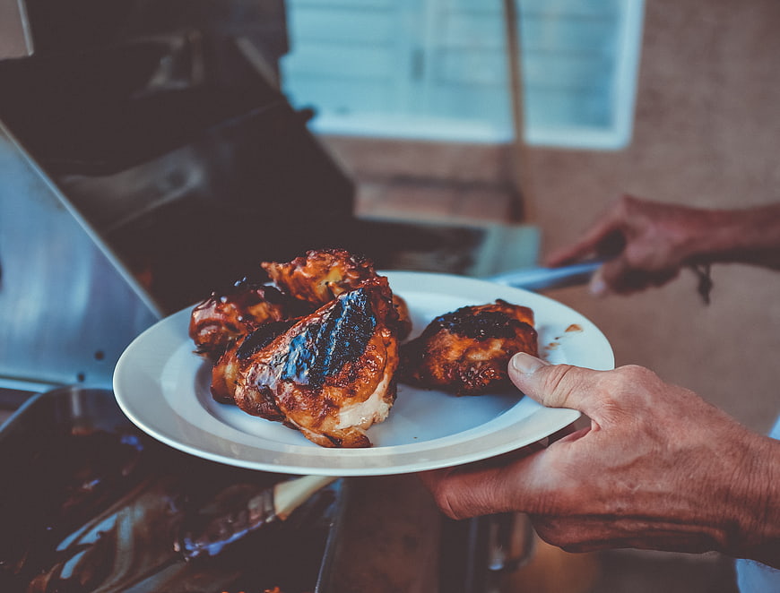 Hands holding plate of grilled chicken near barbecue grill