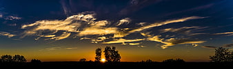 Panoramic sunset with dramatic clouds and tree silhouettes