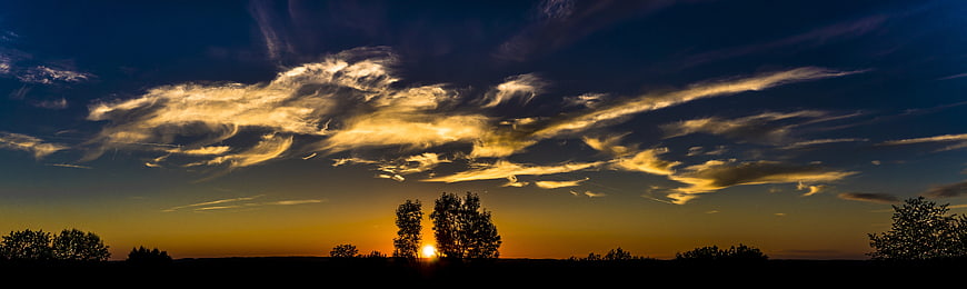 Panoramic sunset with dramatic clouds and tree silhouettes