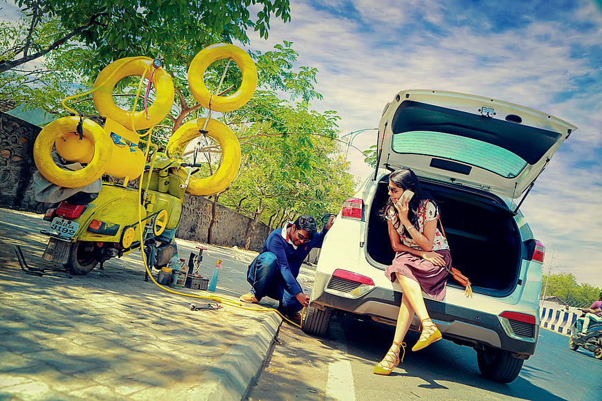 Woman waiting while mechanic fixes car tire roadside