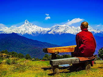 Buddhist monk meditating on wooden bench overlooking Himalayan mountains