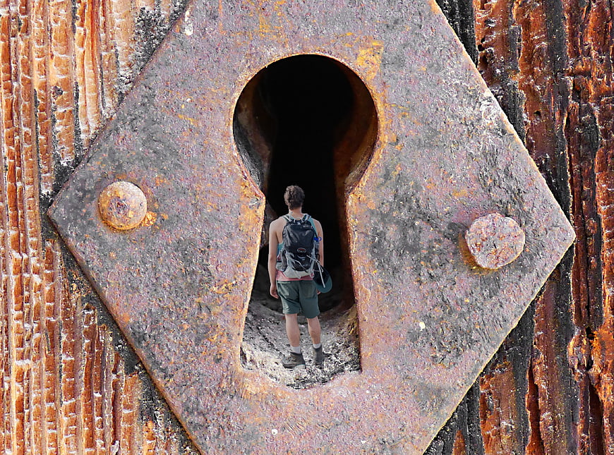 Hiker Entering Rusty Keyhole Doorway In Industrial Wall