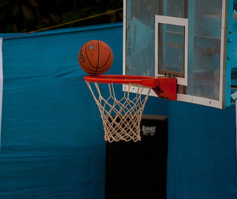 Orange basketball balanced on hoop rim against blue background