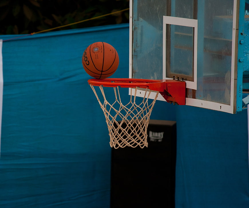 Orange basketball balanced on hoop rim against blue background