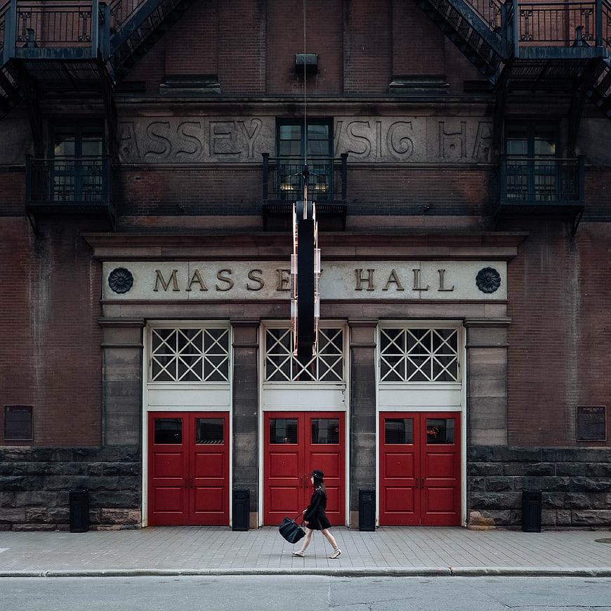 Woman walking past Massey Hall red doors in Toronto