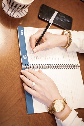 Woman writing in planner with gold watch and coffee