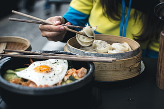 Close-up of hands eating Korean bibimbap and dumplings
