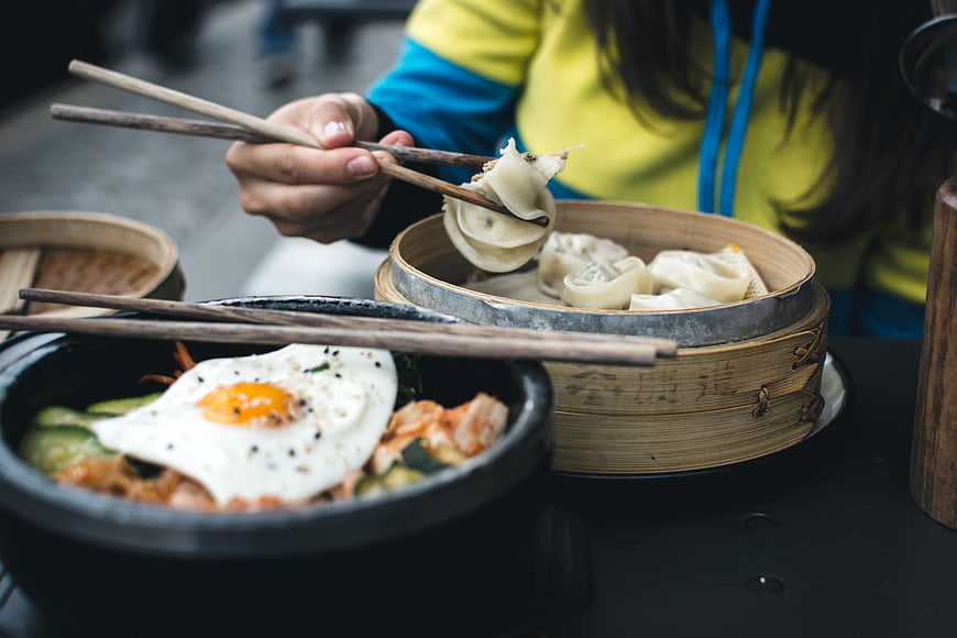 Close-up of hands eating Korean bibimbap and dumplings