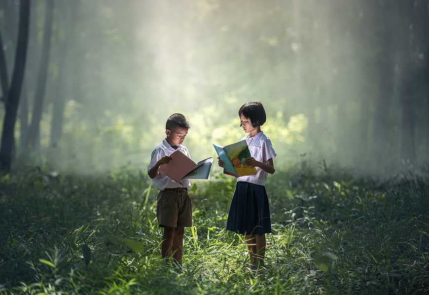 Two Asian school children reading books in a misty forest