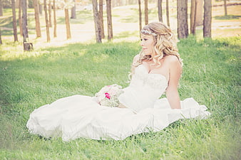 Bride in White Dress Sitting in Grassy Forest with Bouquet