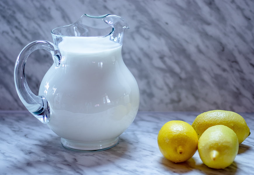 Glass pitcher of milk with fresh lemons on marble