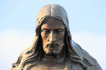 Close-up of a bronze Jesus Christ statue with dewdrops against a blue sky