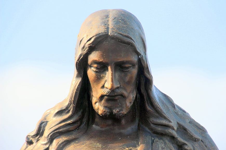 Close-up of a bronze Jesus Christ statue with dewdrops against a blue sky