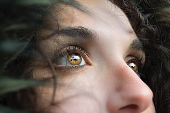 Close-up portrait of a woman's brown eyes looking upward through dark hair