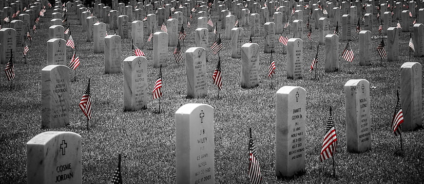 Rows of white headstones with American flags in a military cemetery