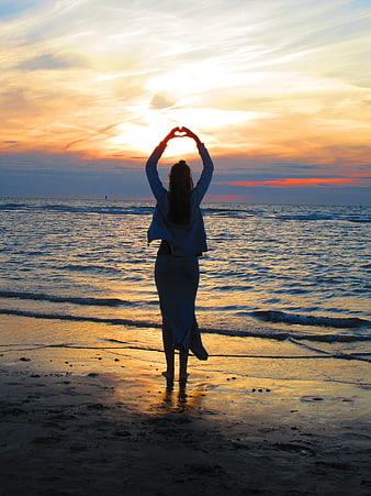 Woman Making Heart Shape Silhouette on Beach at Sunset