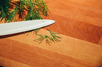 Fresh dill and white ceramic knife on wooden cutting board