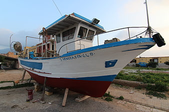 White and blue fishing boat on land in Sicily