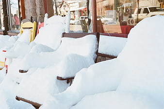 Snow-covered wooden chairs outside a storefront window