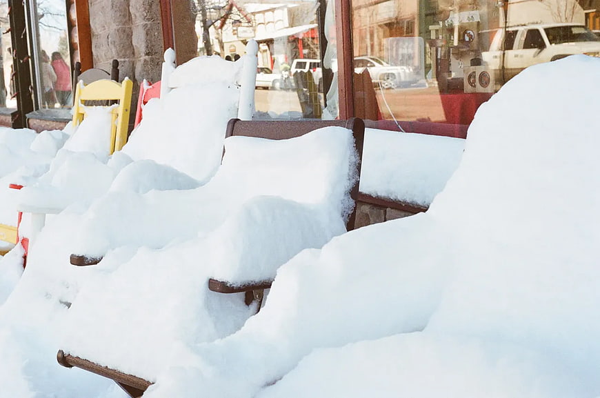 Snow-covered wooden chairs outside a storefront window