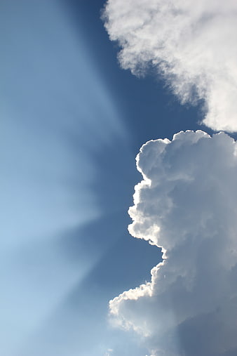 Dramatic Sun Rays Breaking Through Fluffy White Clouds in Blue Sky