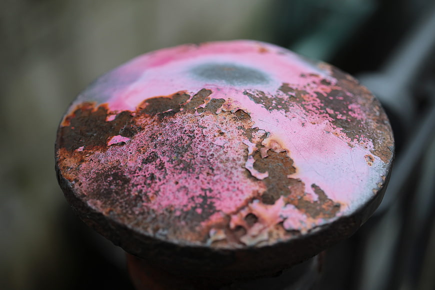 Close-up of rusty metal post with peeling pink paint