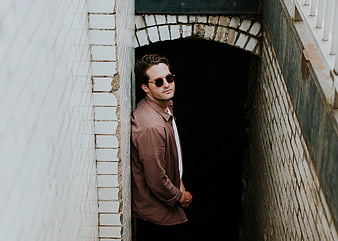 Stylish man in sunglasses leaning against white brick wall
