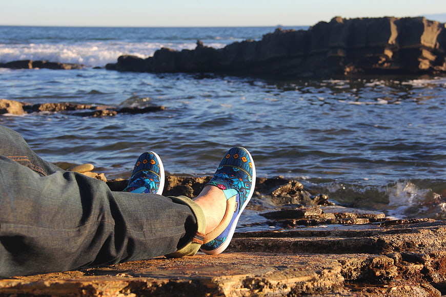 Relaxing feet in blue patterned shoes on rocky beach