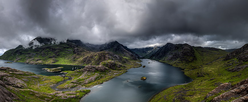 Dramatic panoramic landscape of a fjord with green mountains and stormy clouds