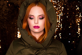 Portrait of a woman with red hair and pink makeup in a green hood