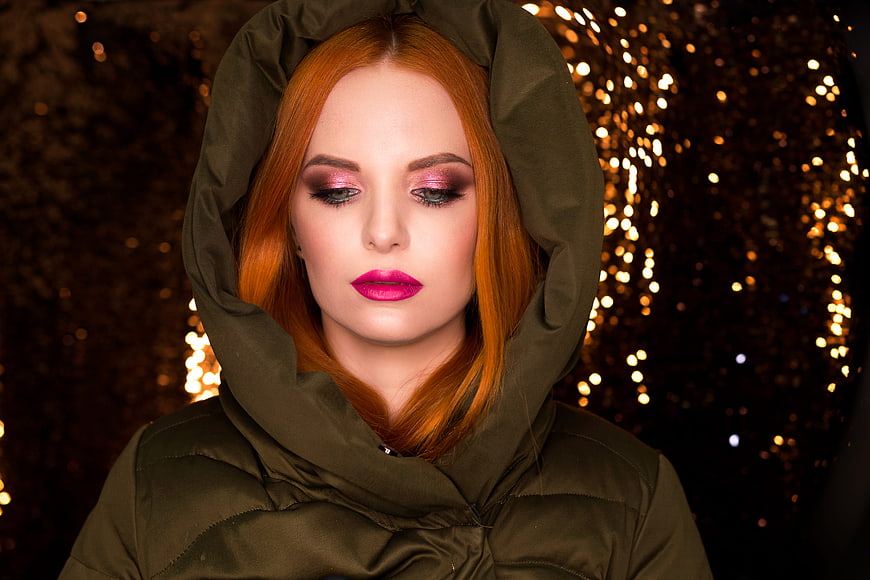 Portrait of a woman with red hair and pink makeup in a green hood