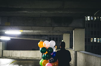 Man holding colorful balloons in dark parking garage