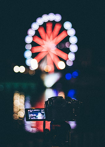 Camera capturing blurred Ferris wheel lights at night